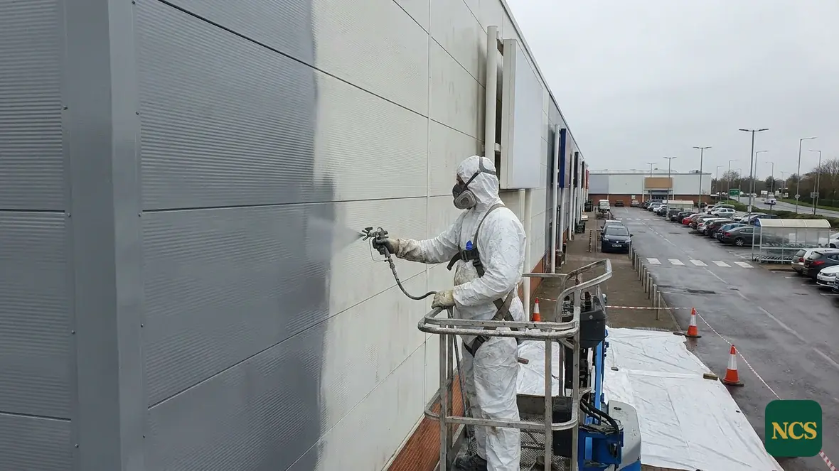 Operative in full PPE spray-coating commercial cladding from a MEWP, cladding spraying in progress