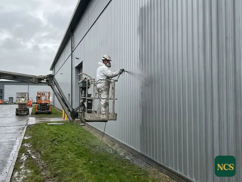 Operative spraying a commercial building from a cherry picker